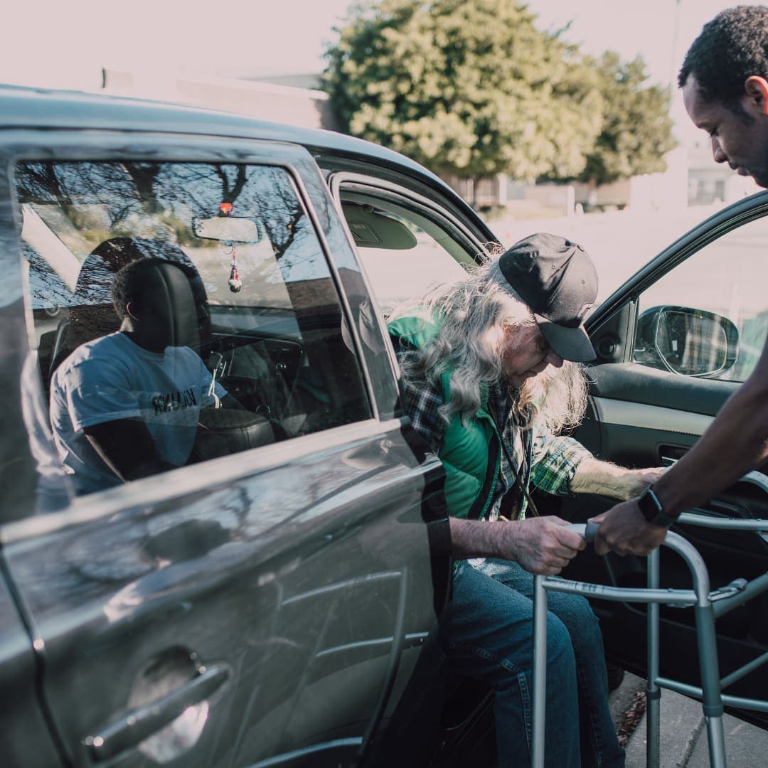 A passenger using a walker being helped out of the car