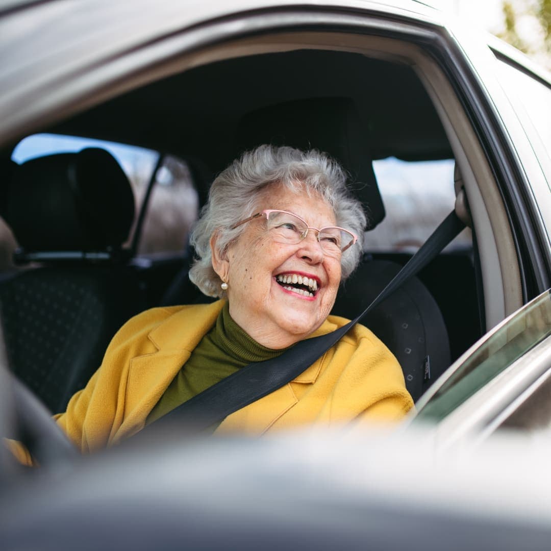 An older passenger laughing in the car, seatbelt on